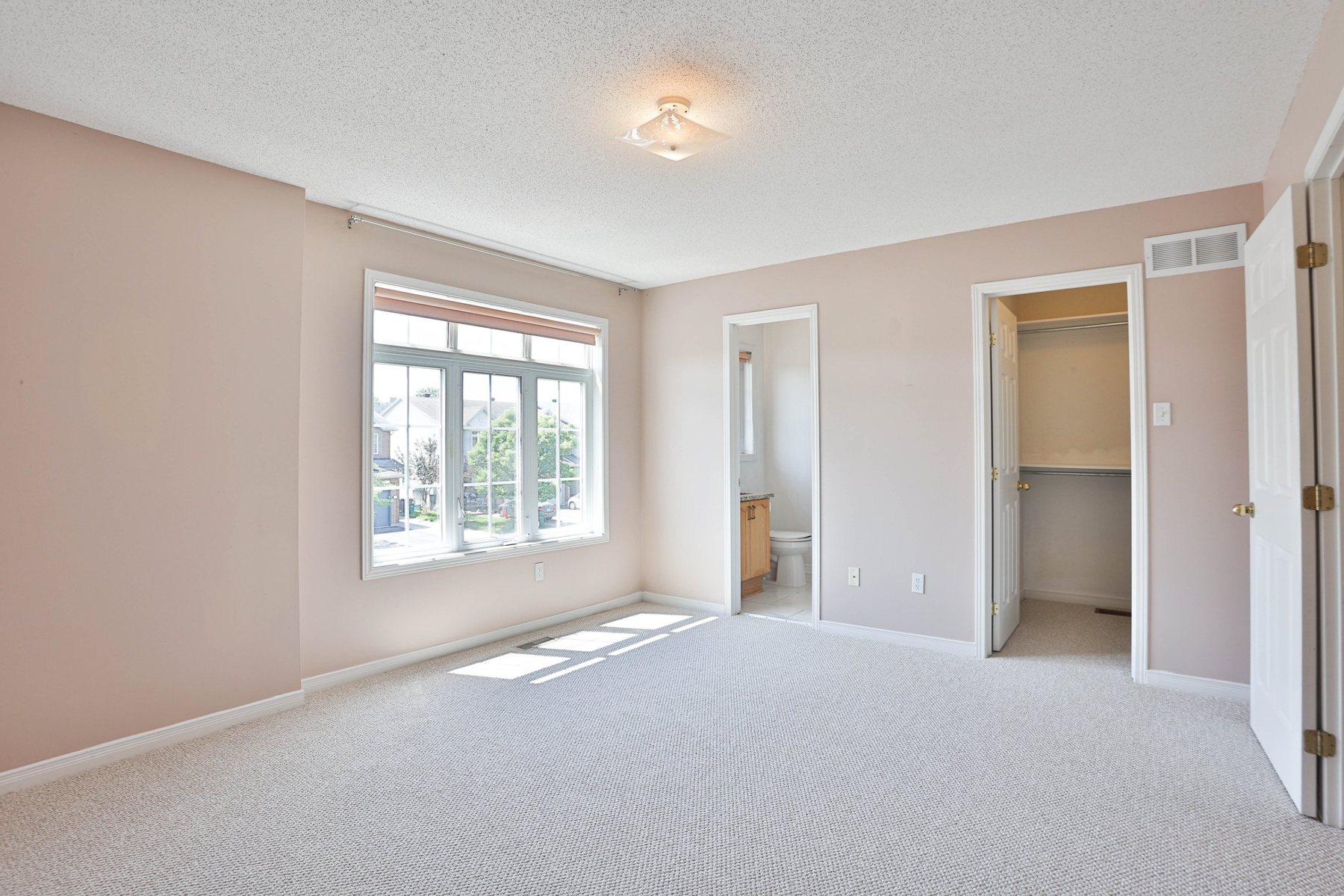 Empty primary bedroom with a bay window, ensuite and walk-in closet