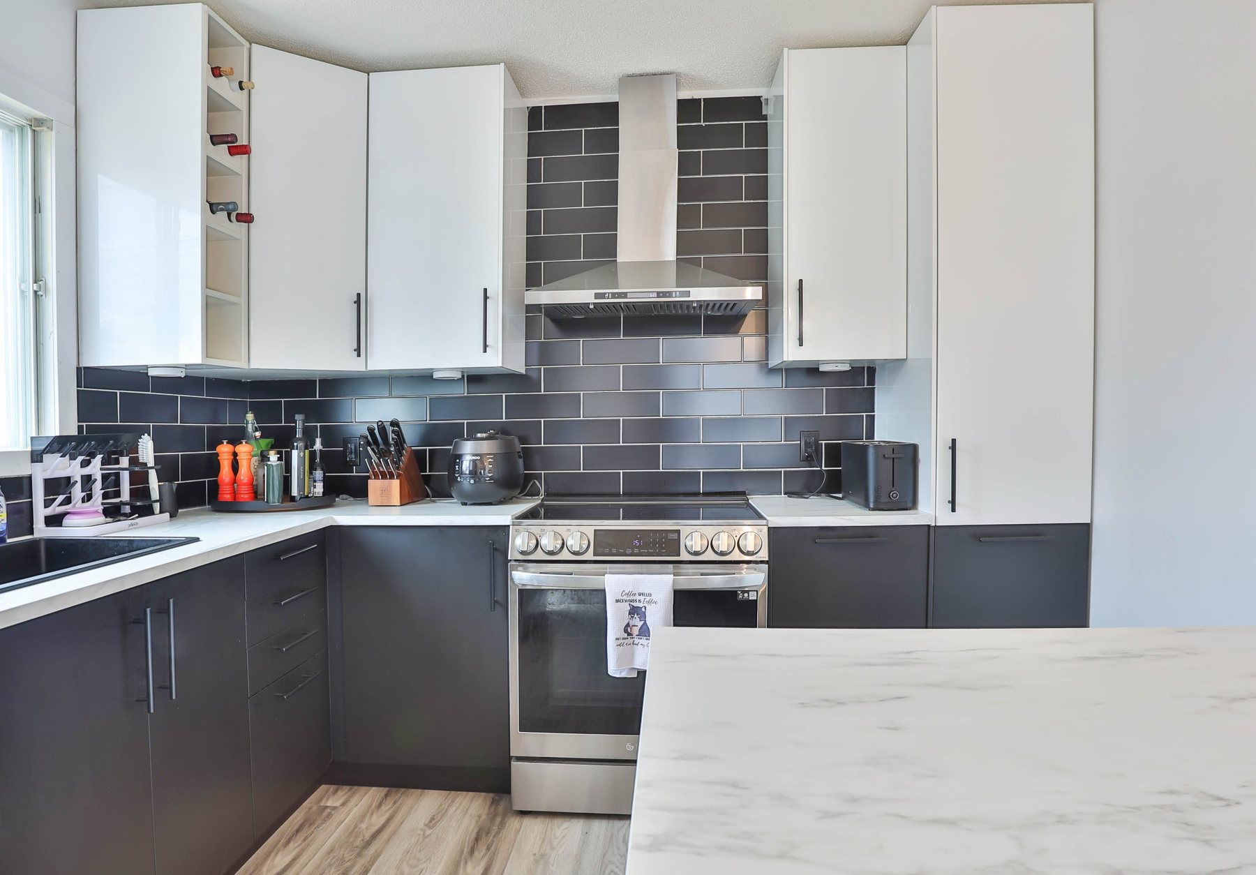 Kitchen with dark subway backsplash, white upper cabinets and a stainless range
